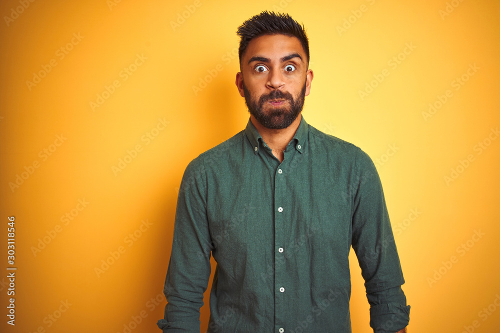 Obraz premium Young indian businessman wearing elegant shirt standing over isolated white background puffing cheeks with funny face. Mouth inflated with air, crazy expression.