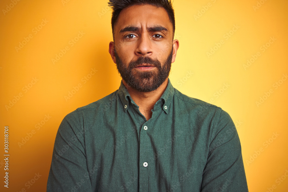 Obraz premium Young indian man wearing green shirt standing over isolated yellow background skeptic and nervous, disapproving expression on face with crossed arms. Negative person.