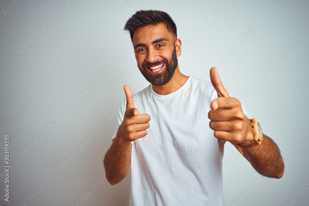 Young indian man wearing t-shirt standing over isolated white background pointing fingers to camera with happy and funny face. Good energy and vibes. Young indian man wearing t-shirt standing over isolated white background pointing fingers to camera with happy and funny face. Good energy and vibes.