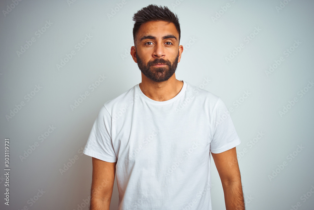 Young indian man wearing t-shirt standing over isolated white background Relaxed with serious expression on face. Simple and natural looking at the camera. Young indian man wearing t-shirt standing over isolated white background Relaxed with serious expression on face. Simple and natural looking at the camera.
