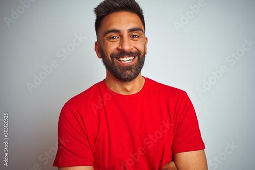 Young indian man wearing red t-shirt over isolated white background happy face smiling with crossed arms looking at the camera. Positive person.