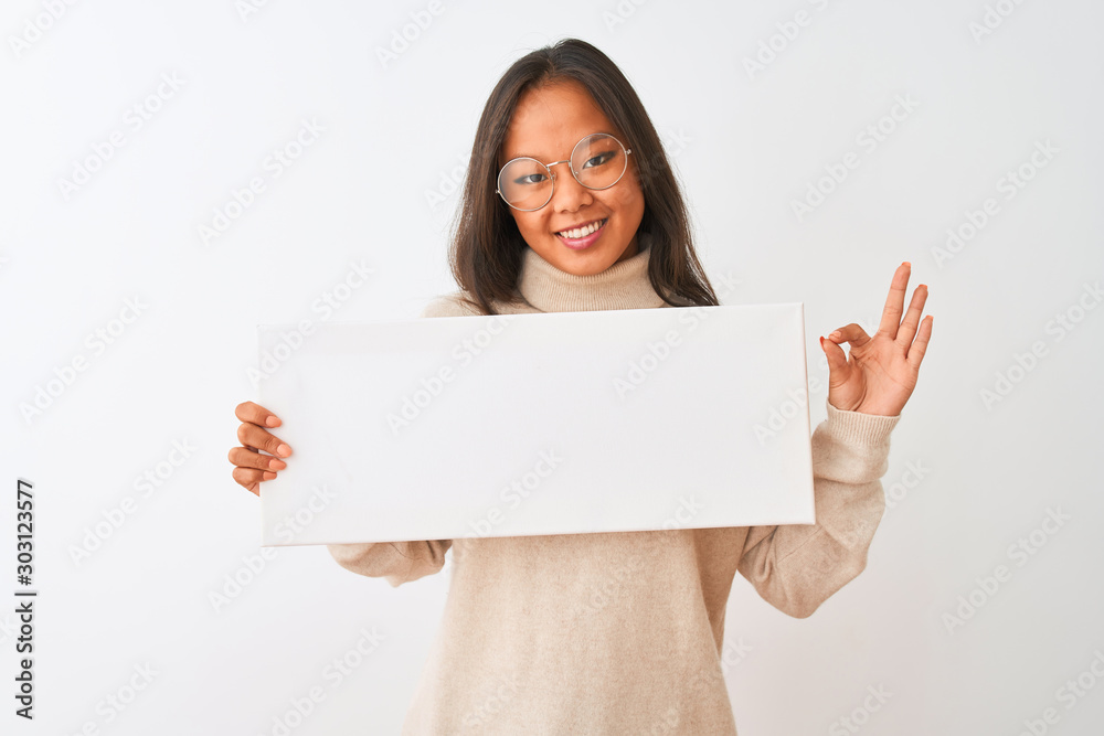 Young beautiful chinese woman wearing glasses holding banner over isolated white background doing ok sign with fingers, excellent symbol Young beautiful chinese woman wearing glasses holding banner over isolated white background doing ok sign with fingers, excellent symbol