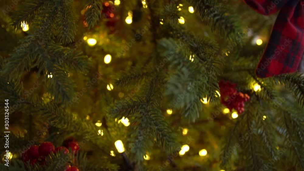 Closeup view of green branches of Christmas tree decorated with red ornaments and golden lights of led garlands.