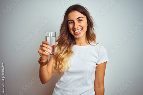 Young beautiful woman drinking a glass of water over white isolated background with a happy face standing and smiling with a confident smile showing teeth