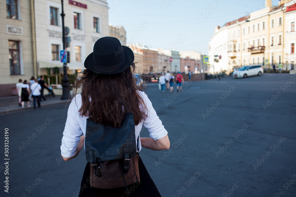 Young woman in hat walking in city, back view. Girl tourist enjoys the walk.