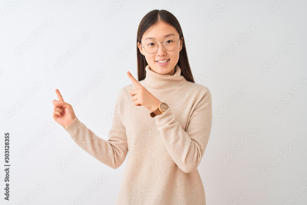 Young chinese woman wearing turtleneck sweater and glasses over isolated white background smiling and looking at the camera pointing with two hands and fingers to the side. Young chinese woman wearing turtleneck sweater and glasses over isolated white background smiling and looking at the camera pointing with two hands and fingers to the side.