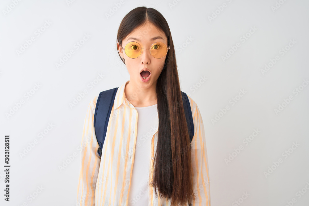 Young chinese student woman wearing glasses and backpack over isolated white background afraid and shocked with surprise expression, fear and excited face. - obrazy, fototapety, plakaty 