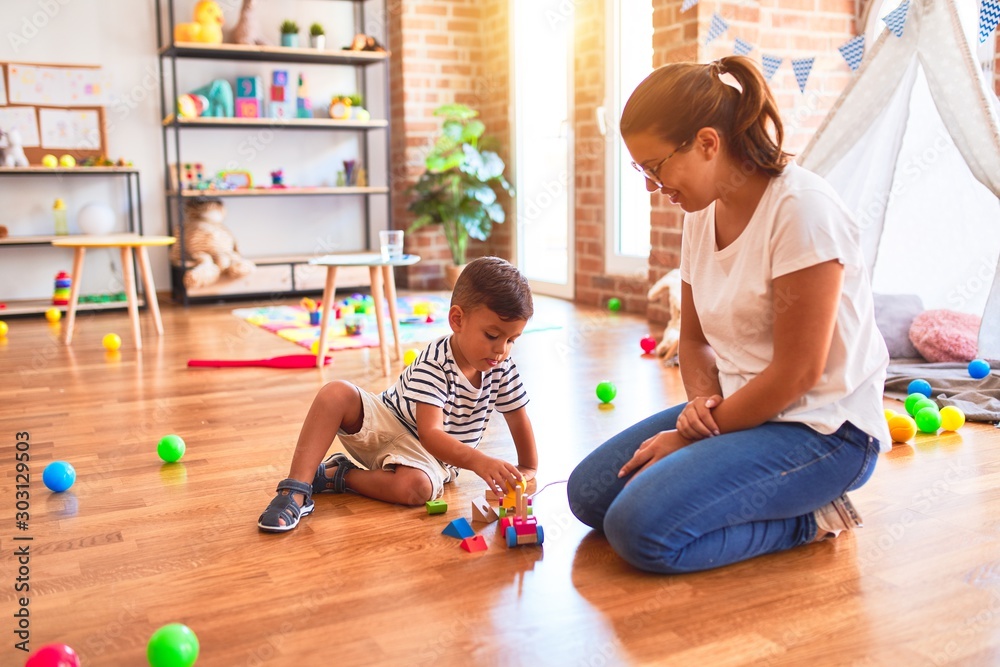 Fototapeta premium Beautiful teacher and toddler boy playing with train at kindergarten