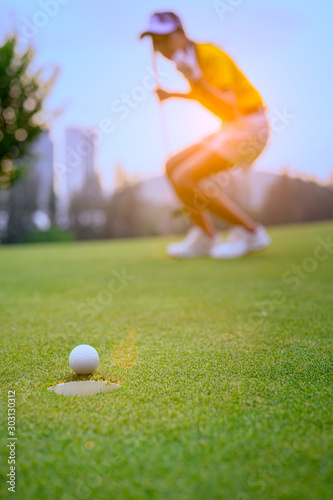 young woman golf player mostly success to putting golf ball into the hole on the green of the golf course, cheerfully of woman golf player in background