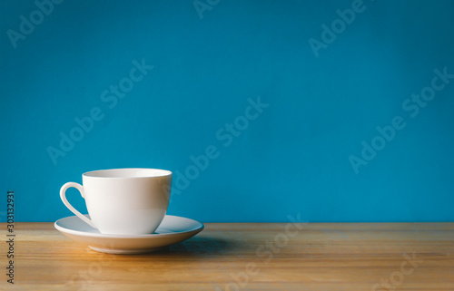 фотографія white cup of coffee on wooden table with blue background