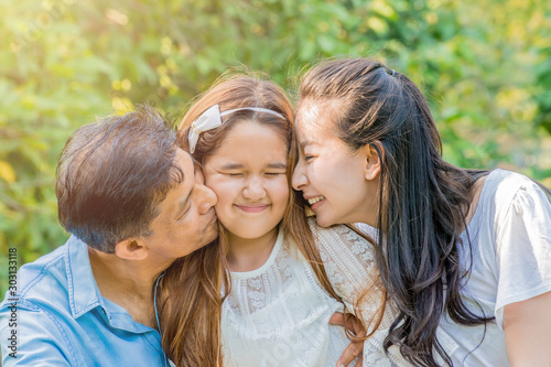 Asian parents kissing their daughter in the cheeks outdoor.