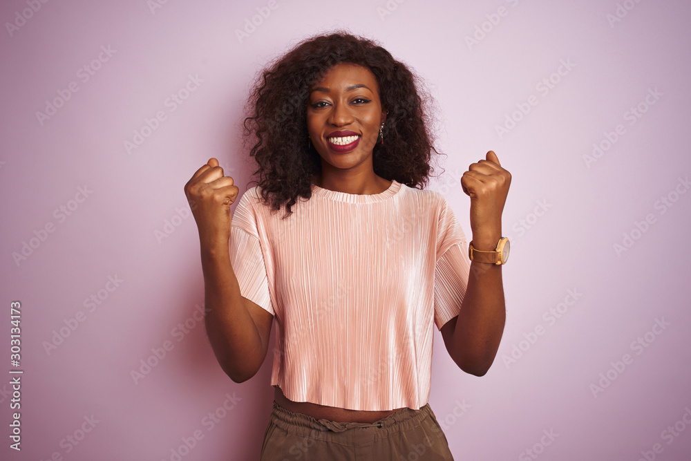 Young african american woman wearing t-shirt standing over isolated pink background celebrating surprised and amazed for success with arms raised and open eyes. Winner concept. Young african american woman wearing t-shirt standing over isolated pink background celebrating surprised and amazed for success with arms raised and open eyes. Winner concept.