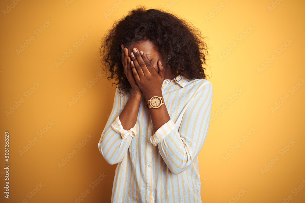 African american woman wearing striped shirt standing over isolated yellow background with sad expression covering face with hands while crying. Depression concept. African american woman wearing striped shirt standing over isolated yellow background with sad expression covering face with hands while crying. Depression concept.