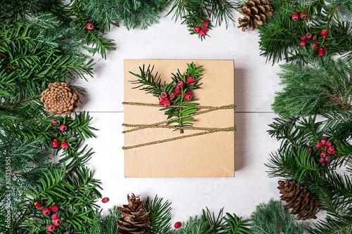 Christmas gift box and fir tree branches with red berries on wooden background.