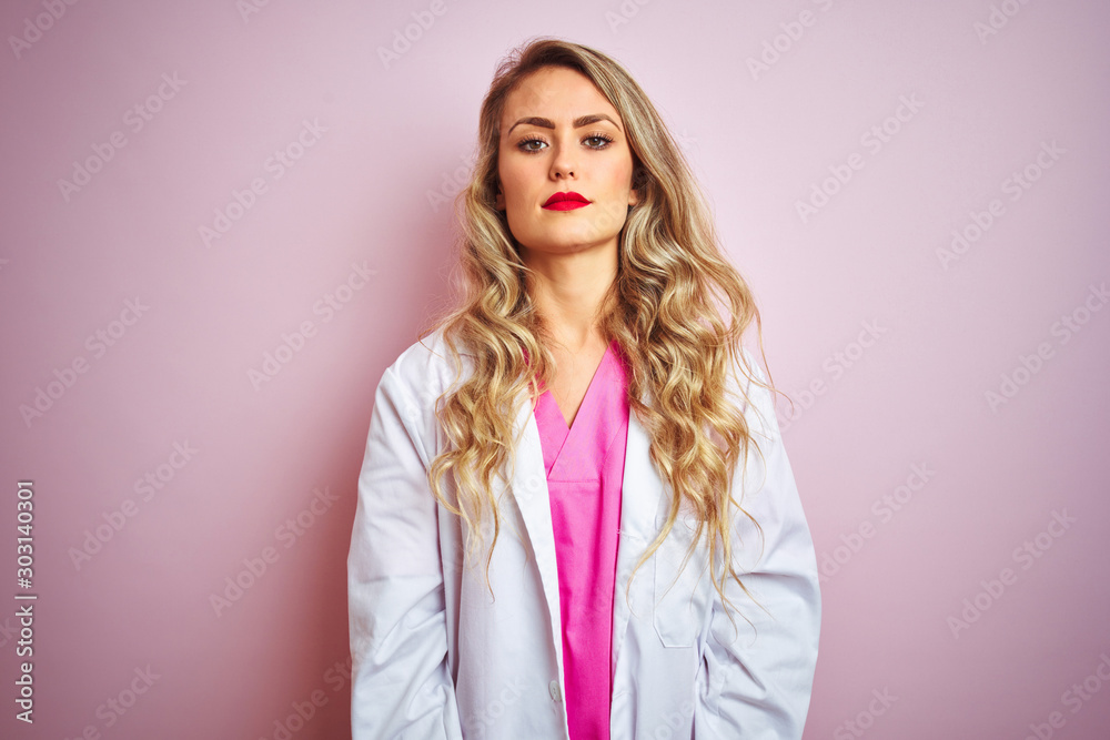 Young beautiful doctor woman standing over pink isolated background with serious expression on face. Simple and natural looking at the camera. Young beautiful doctor woman standing over pink isolated background with serious expression on face. Simple and natural looking at the camera.