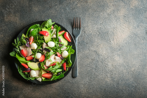 Salad with fresh strawberries, mozzarella, chicken, avocado and fresh herbs on a dark plate on a dark background.