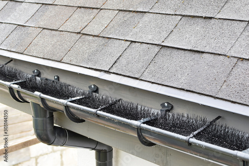 Plastic guard brush in new dark grey plastic rain gutter on asphalt shingles roof.