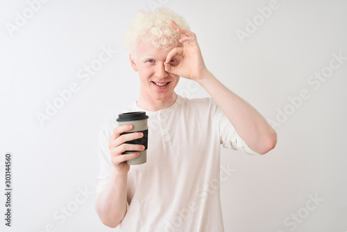Young albino blond man drinking coffee standing over isolated white background with happy face smiling doing ok sign with hand on eye looking through fingers