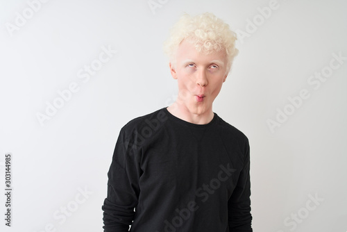 Young albino blond man wearing black t-shirt standing over isolated white background making fish face with lips, crazy and comical gesture. Funny expression.