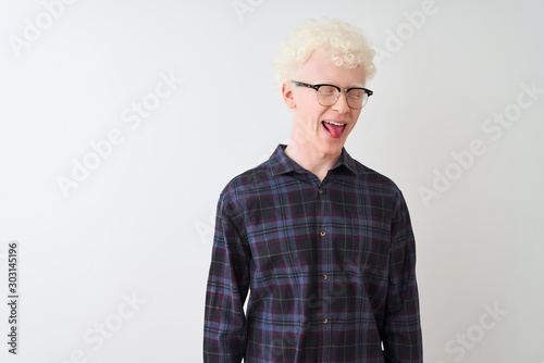 Young albino blond man wearing casual shirt and glasses over isolated white background sticking tongue out happy with funny expression. Emotion concept.