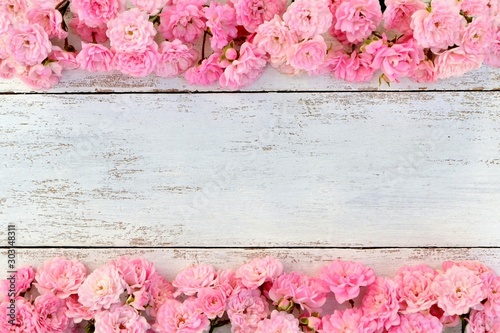 Frame with small delicate pink roses on white wooden background