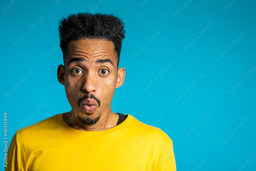Amazed mixed race man shocked, saying WOW. Handsome african american guy with afro hair surprised to camera over blue background. Copy space. Amazed mixed race man shocked, saying WOW. Handsome african american guy with afro hair surprised to camera over blue background. Copy space.