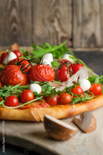 Traditional italian pizza with cherry tomatoes on a wooden shovel on a dark background.