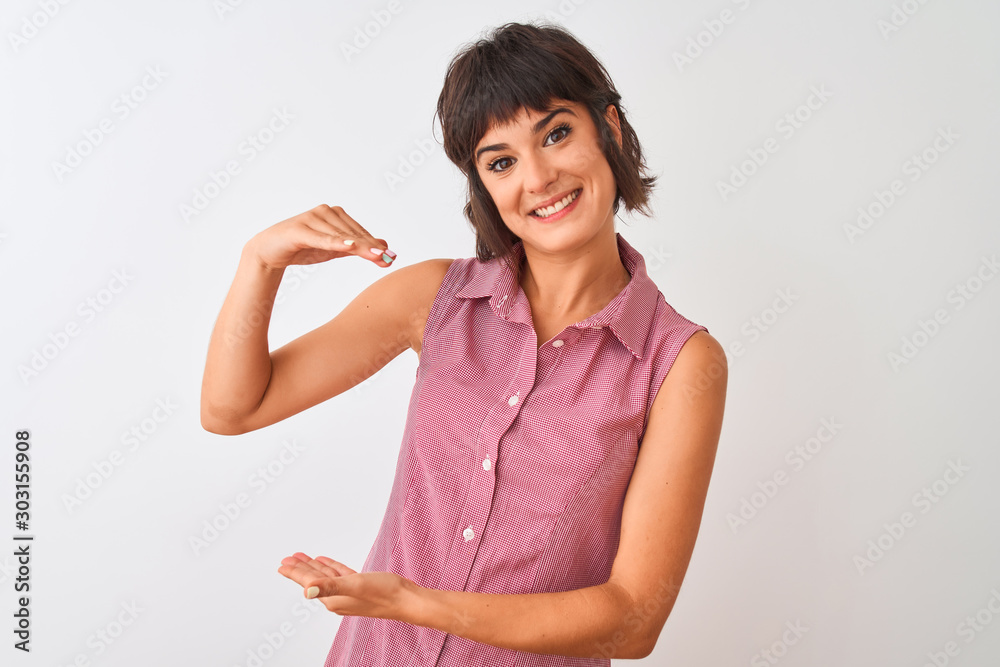Young beautiful woman wearing red summer shirt standing over isolated white background gesturing with hands showing big and large size sign, measure symbol. Smiling looking at the camera. Measuring Young beautiful woman wearing red summer shirt standing over isolated white background gesturing with hands showing big and large size sign, measure symbol. Smiling looking at the camera. Measuring