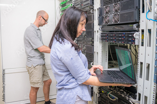 A team of experts working near the computer racks datacenter. Man and woman set up network equipment in the server room. Teamwork concept in the field of information technology.
