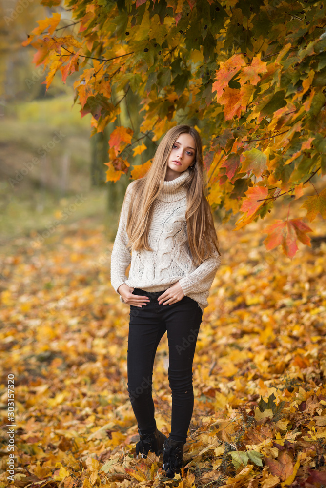 pensive young long haired girl in a light sweater against the background of yellow autumn trees