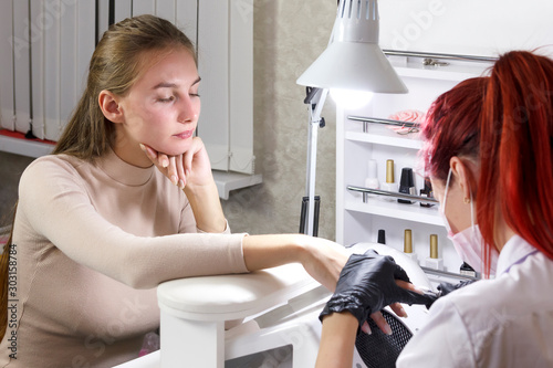 A manicurist in a beauty parlor makes a client a hardware manicure preparing for gel coating. photo