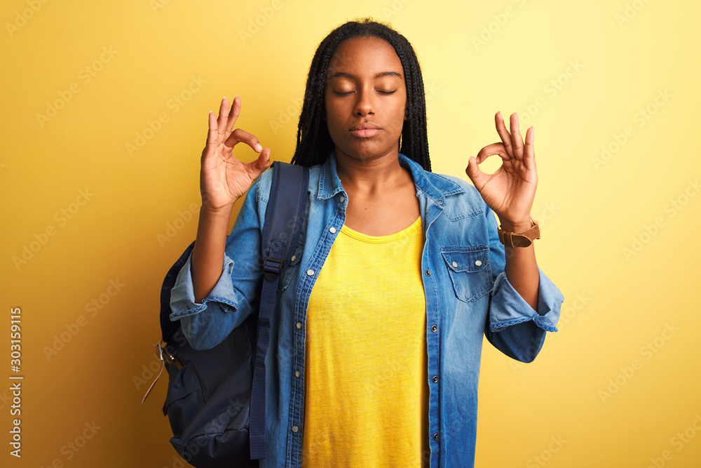 African american student woman wearing backpack standing over isolated yellow background relax and smiling with eyes closed doing meditation gesture with fingers. Yoga concept. African american student woman wearing backpack standing over isolated yellow background relax and smiling with eyes closed doing meditation gesture with fingers. Yoga concept.