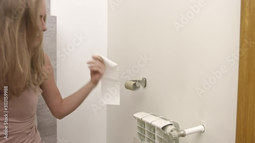 A woman is sitting on a toilet and running out of toilet paper