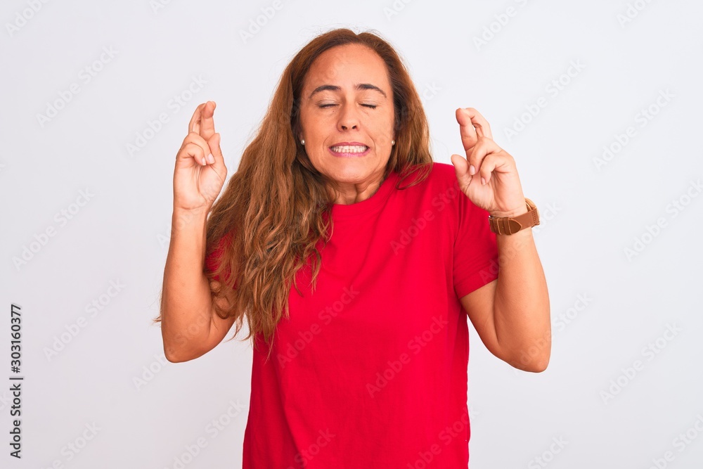 Middle age mature woman standing over white isolated background gesturing finger crossed smiling with hope and eyes closed. Luck and superstitious concept. Middle age mature woman standing over white isolated background gesturing finger crossed smiling with hope and eyes closed. Luck and superstitious concept.