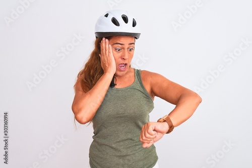 Middle age mature cyclist woman wearing safety helmet over isolated background Looking at the watch time worried, afraid of getting late © Krakenimages.com