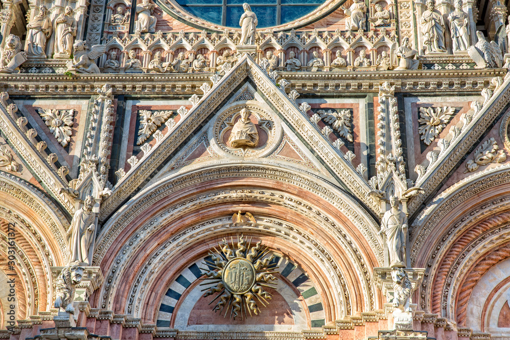 Siena Cathedral is a famous Italian romanesque-gothic cathedral with a striking facade is crowded with sculptures and architectural details and capped by a bronze sun, Tuscany, Italy