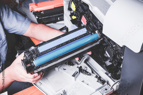 Business man or technician is checking and changing the printer equipment cartridges tone of laser jet multi function printer in the office. Close-up shot of CMYK ink cartridges for laser printer.