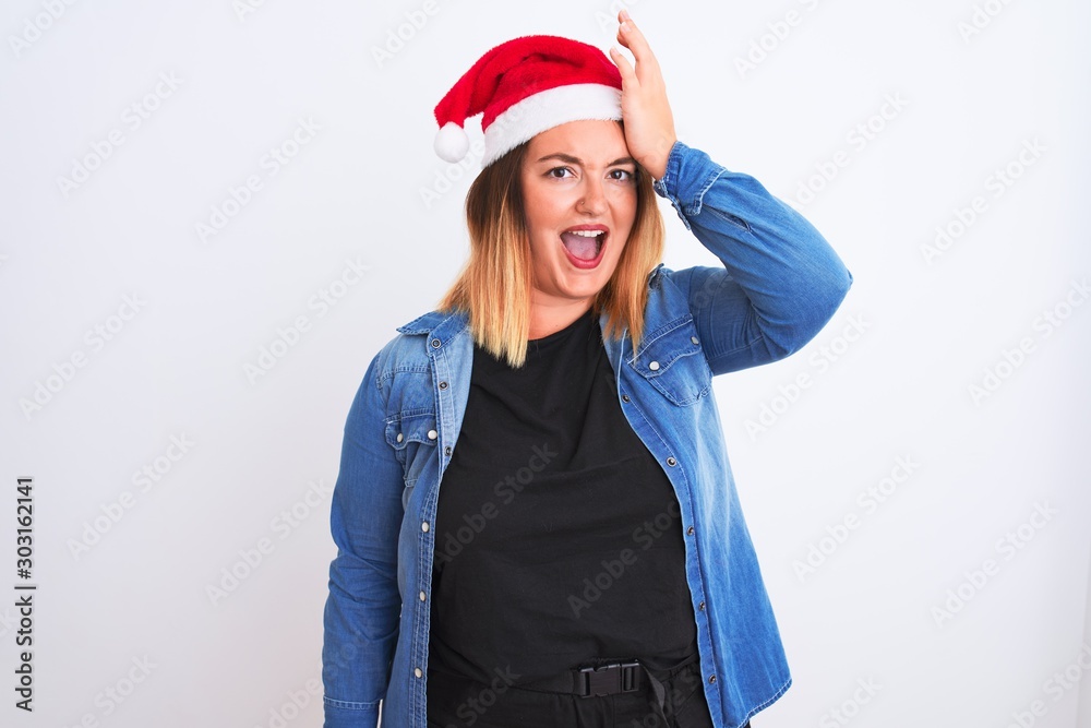 Young beautiful woman wearing Christmas Santa hat standing over isolated white background surprised with hand on head for mistake, remember error. Forgot, bad memory concept. Young beautiful woman wearing Christmas Santa hat standing over isolated white background surprised with hand on head for mistake, remember error. Forgot, bad memory concept.