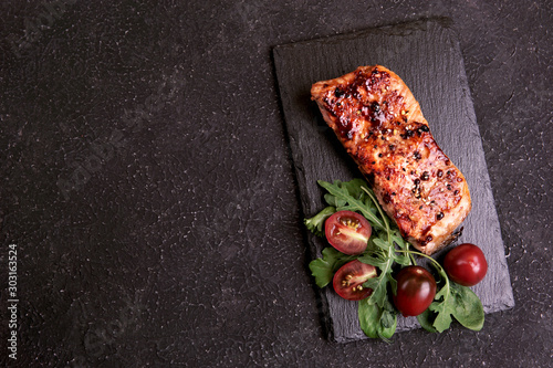 Fried teriyaki salmon with spices, sesame, green salad and tomatoes on stone plate, black textured background. Top view, flat lay, copy space. 