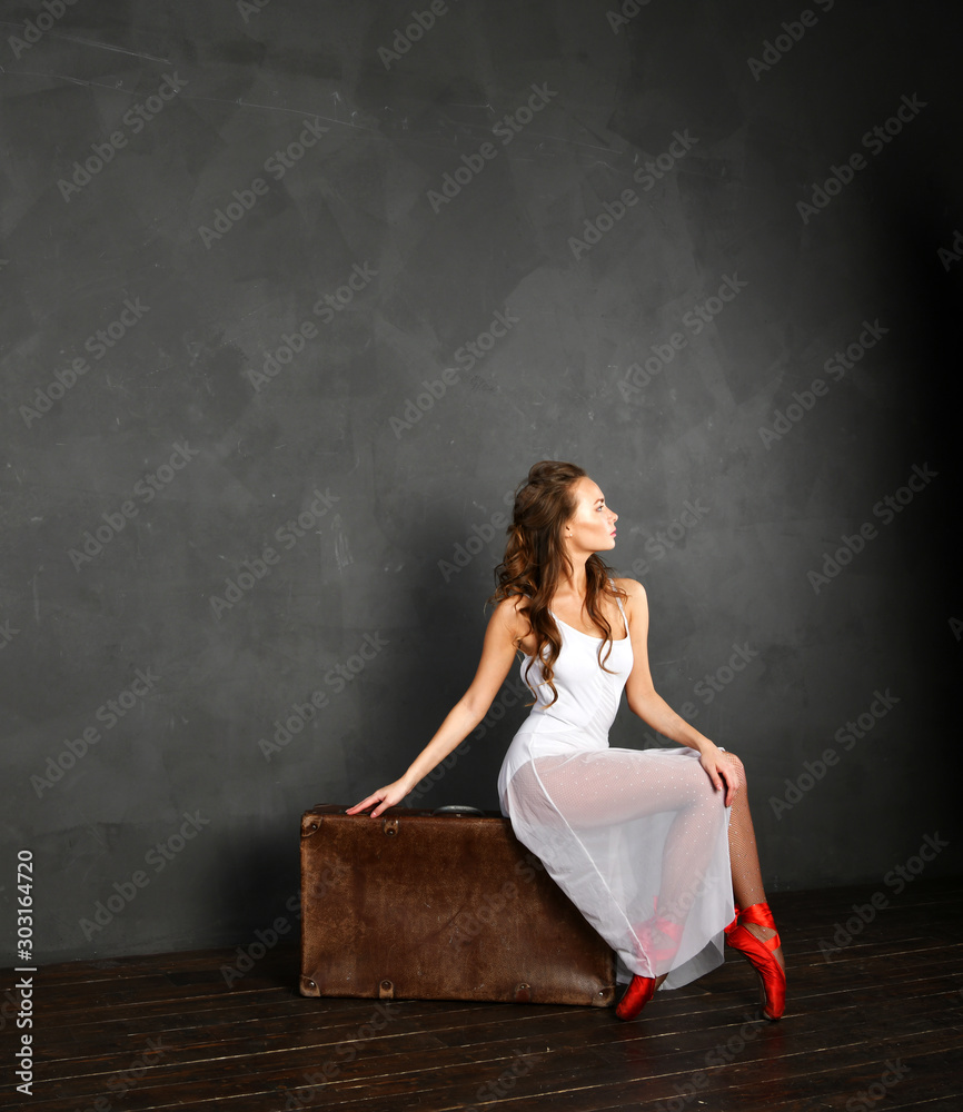 girl in a white transparent dress in red pointe shoes on a brown suitcase girl in a white transparent dress in red pointe shoes on a brown suitcase