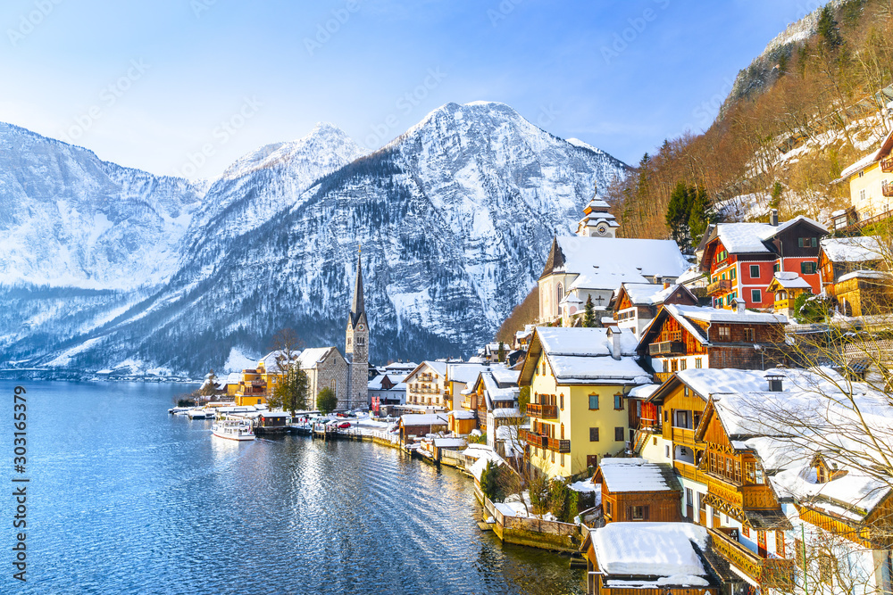 Classic postcard view of famous Hallstatt lakeside town in the Alps with traditional passenger ship on a beautiful cold sunny day with blue sky and clouds in winter, Salzkammergut region, Austria