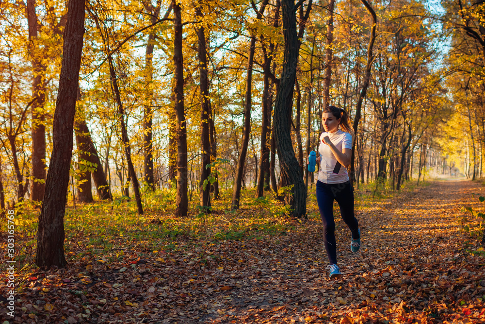 Runner exercising in autumn park. Woman running with water bottle at sunset. Active lifestyle Runner exercising in autumn park. Woman running with water bottle at sunset. Active lifestyle