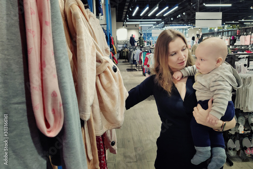Slender pretty woman with a child in her arms chooses clothes in a fashion boutique. Sale concept. Black Friday