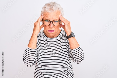 Senior grey-haired woman wearing striped navy t-shirt glasses over isolated white background with hand on head for pain in head because stress. Suffering migraine.