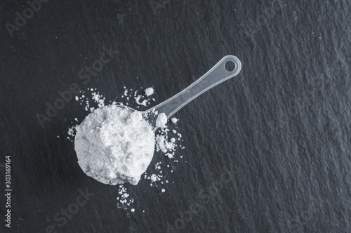 White sports nutrition powder. Soluble creatine in a measuring spoon to increase athlete's stamina and strength. On a stone gray background. photo
