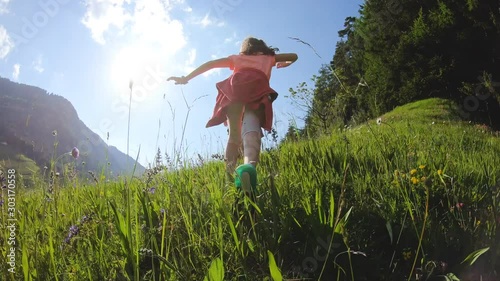 Dolomiti, Italy. Two little girls running on a mountain hill in high green grass. Blue sky on sunny summer day. Wide angle.