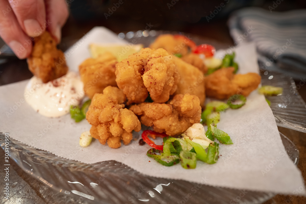 Crispy salt and pepper breaded squid with a lemon mayonnaise dip plus chilli, spring onion and corriander salad on a glass plate. A man is dipping one of the goujons. Crispy salt and pepper breaded squid with a lemon mayonnaise dip plus chilli, spring onion and corriander salad on a glass plate. A man is dipping one of the goujons.