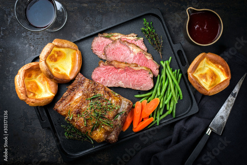 Traditional Commonwealth Sunday roast with sliced cold cuts roast beef with vegetable and Yorkshire pudding as top view on a modern design cast iron tray