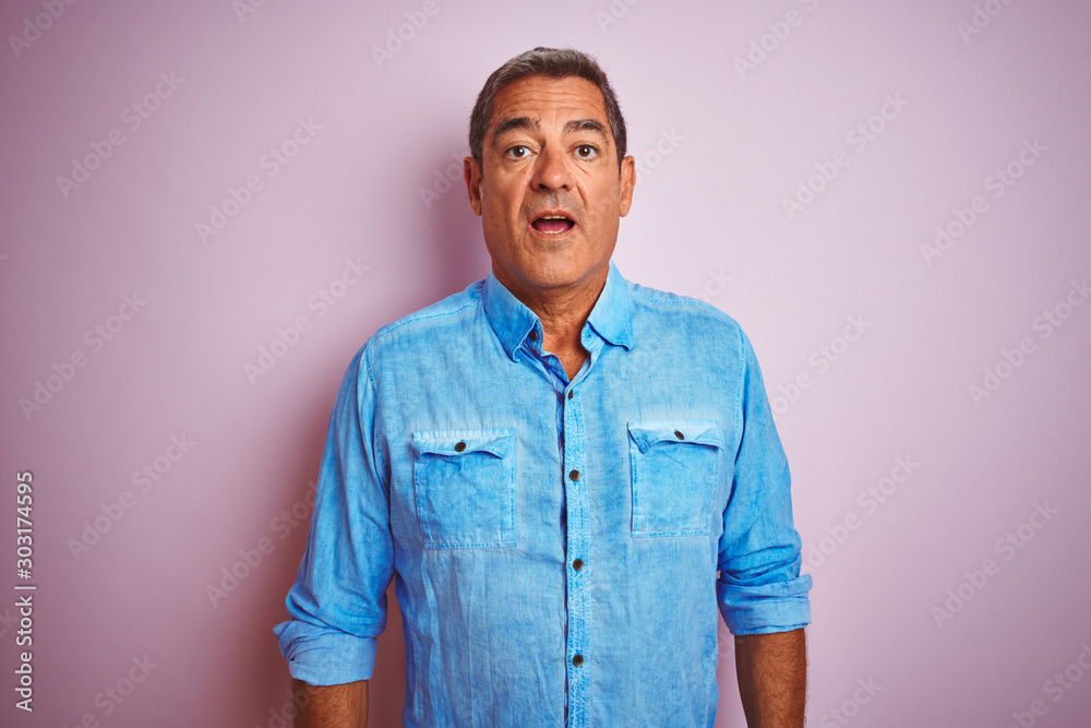 Fototapeta premium Handsome middle age man wearing blue denim shirt standing over isolated pink background scared in shock with a surprise face, afraid and excited with fear expression