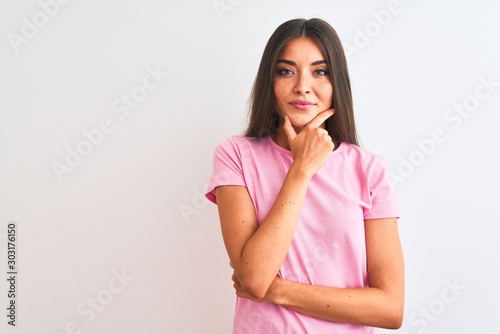 Young beautiful woman wearing pink casual t-shirt standing over isolated white background looking confident at the camera with smile with crossed arms and hand raised on chin. Thinking positive.